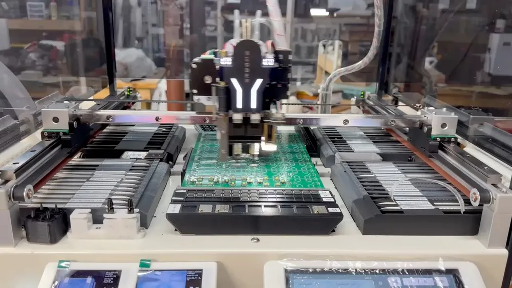 A pick-and-place machine mid-placement over a panel of circuit boards, component feeders racked along both sides.